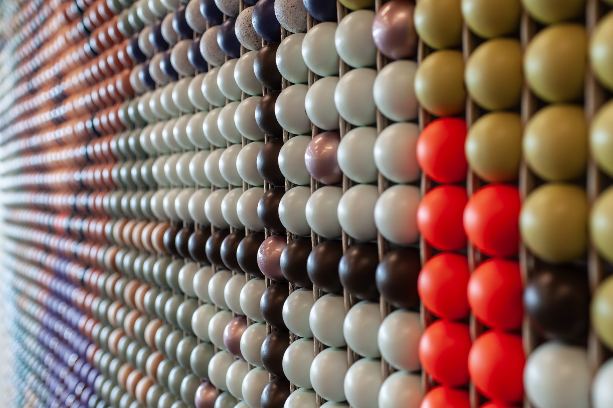 Close view of a woven wall of painted wooden beads by Adam A. Wier